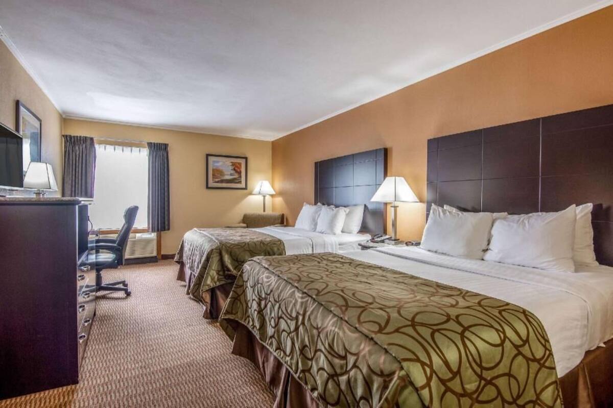 A hotel room with two beds, a desk, a chair, and a television.