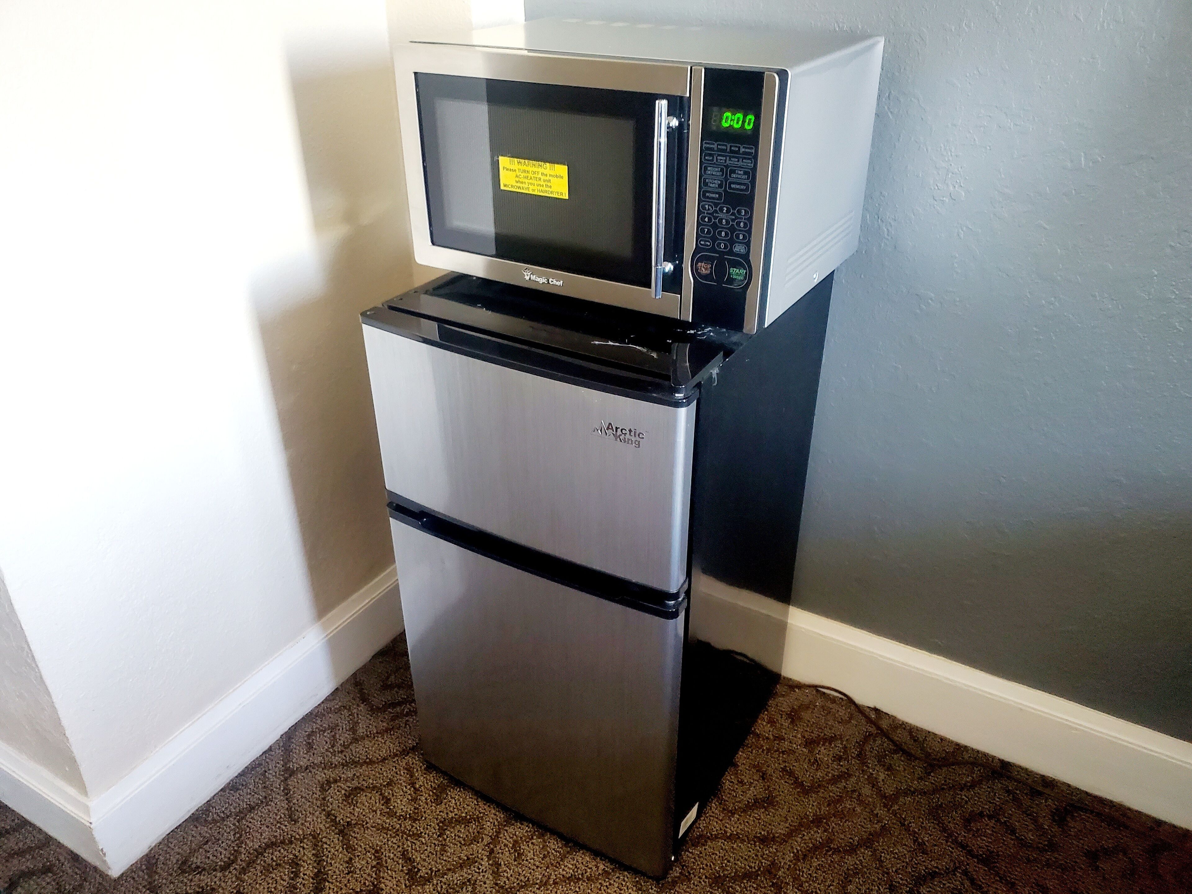 A compact refrigerator with a microwave on top, placed in a corner with a patterned carpet.