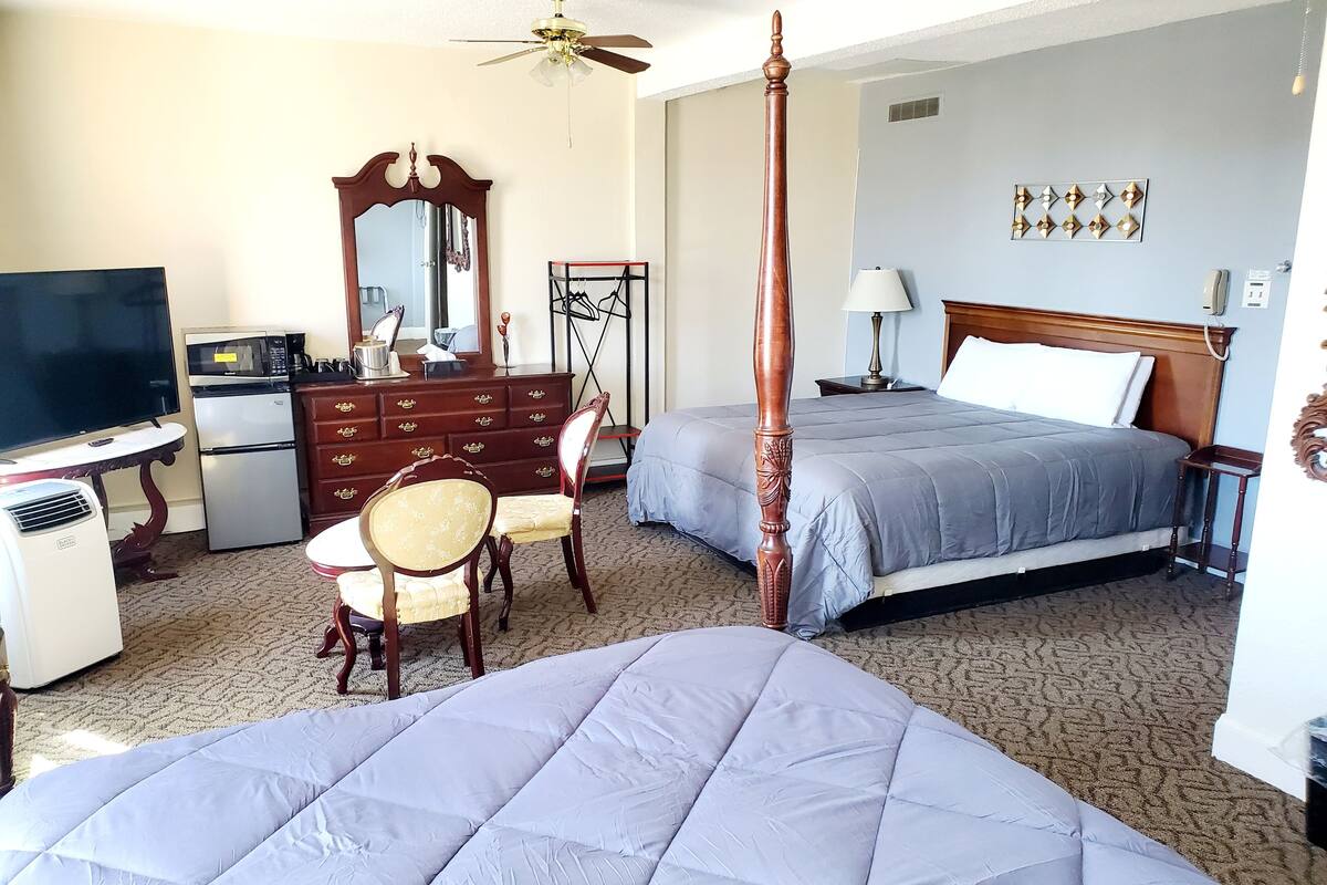 A hotel room with a bed, a desk with a television, a dresser, a chair, and a ceiling fan.
