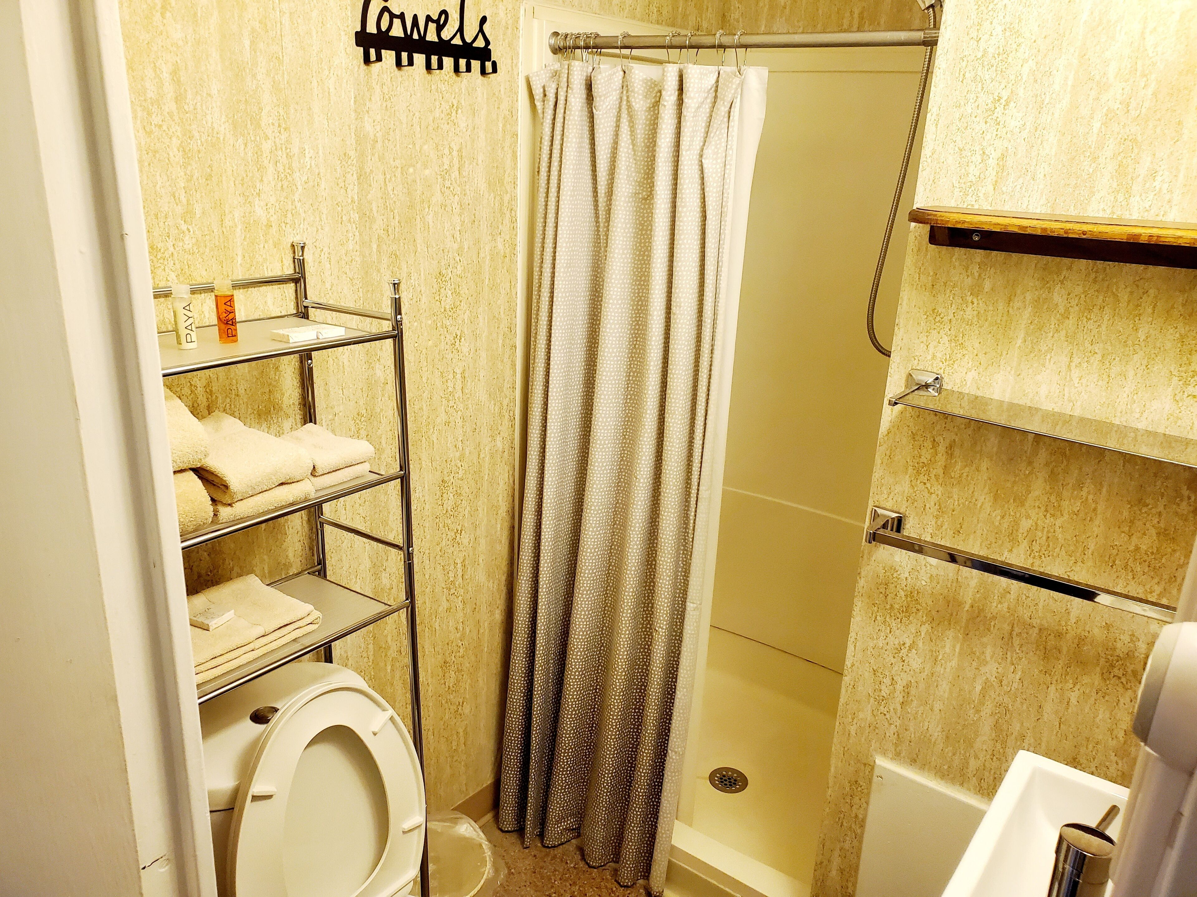 Un baño con inodoro, ducha y un perchero con toallas dobladas.