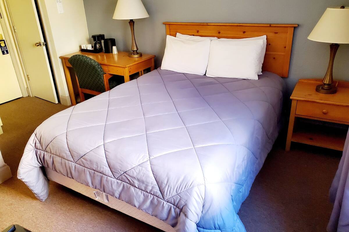 A neatly made bed with a quilted cover, two bedside tables with lamps, a wooden headboard, and a chair.