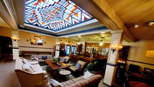 A spacious lobby with a high ceiling, a central seating area with couches and a coffee table, and a bar area with stools. - Monte Villa Hotel (Monte Vista)