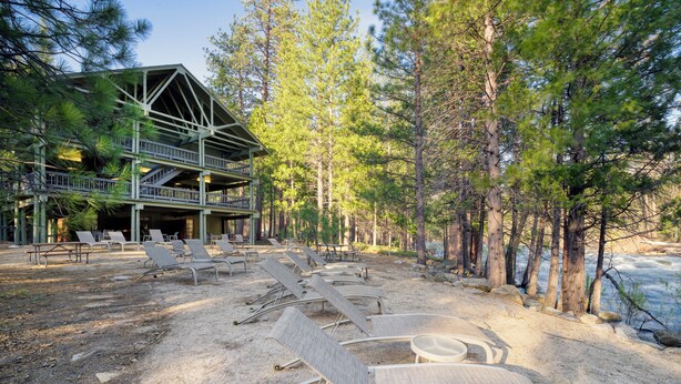 Een lodge met terras, uitkijkend op een rivier, omringd door dennenbomen.
