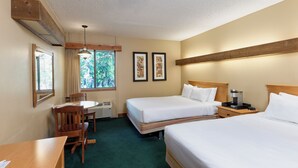 Een hotelkamer met twee bedden, een bureau, een stoel, een raam met uitzicht op bomen en een plafondventilator.