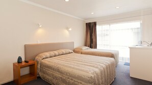 A hotel room with two beds, a small wooden nightstand, a desk, and a window with curtains. - Colonial Inn Motel (Christchurch)