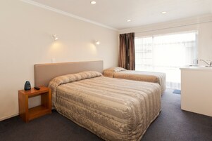 A hotel room with two beds, a small wooden nightstand, a desk, and a window with curtains.