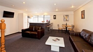 A modern living room with a brown leather sofa, a white coffee table, and a dining area with a small round table and chairs. - Colonial Inn Motel (Christchurch)