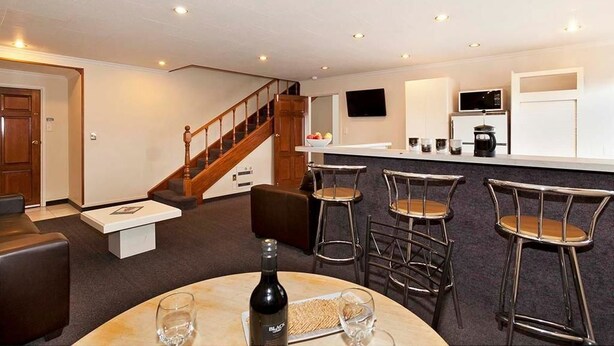 A modern kitchen with a bar area, a staircase, and a seating area with a round table and chairs. - Colonial Inn Motel (Christchurch)