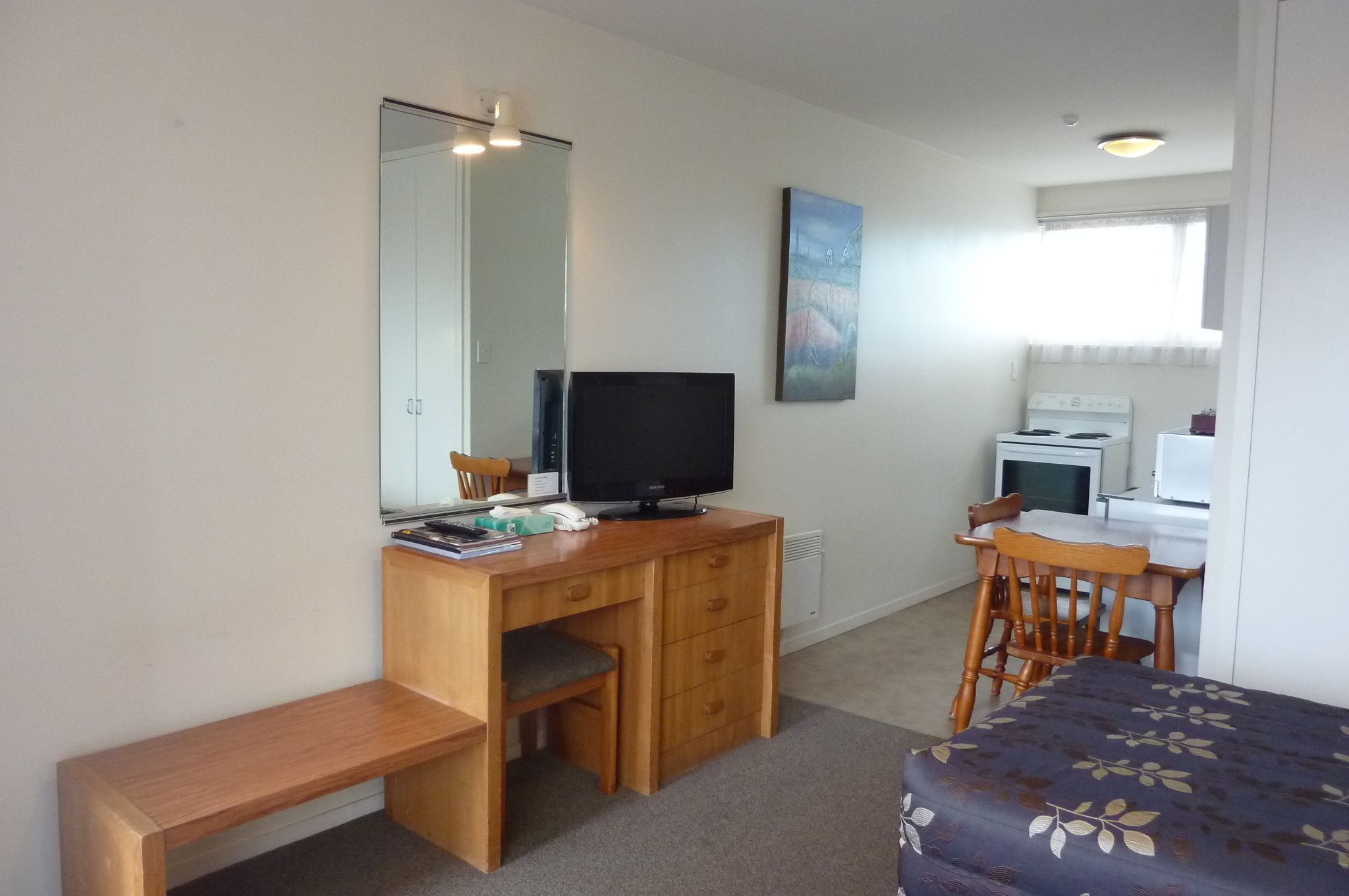 A compact room with a wooden desk, a television, a chair, a small table, and a bed with a floral bedspread.