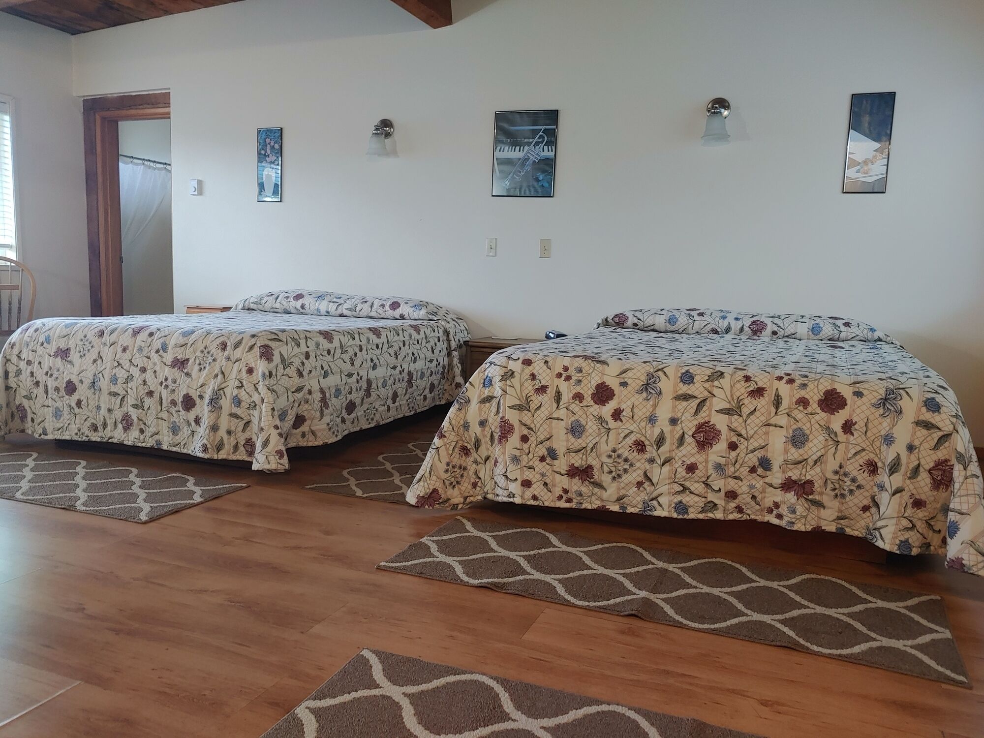 Dos camas individuales con ropa de cama floral, piso de madera y una puerta que da a otra habitación.