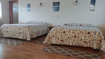 Dos camas individuales con ropa de cama floral, piso de madera y una puerta que da a otra habitación.