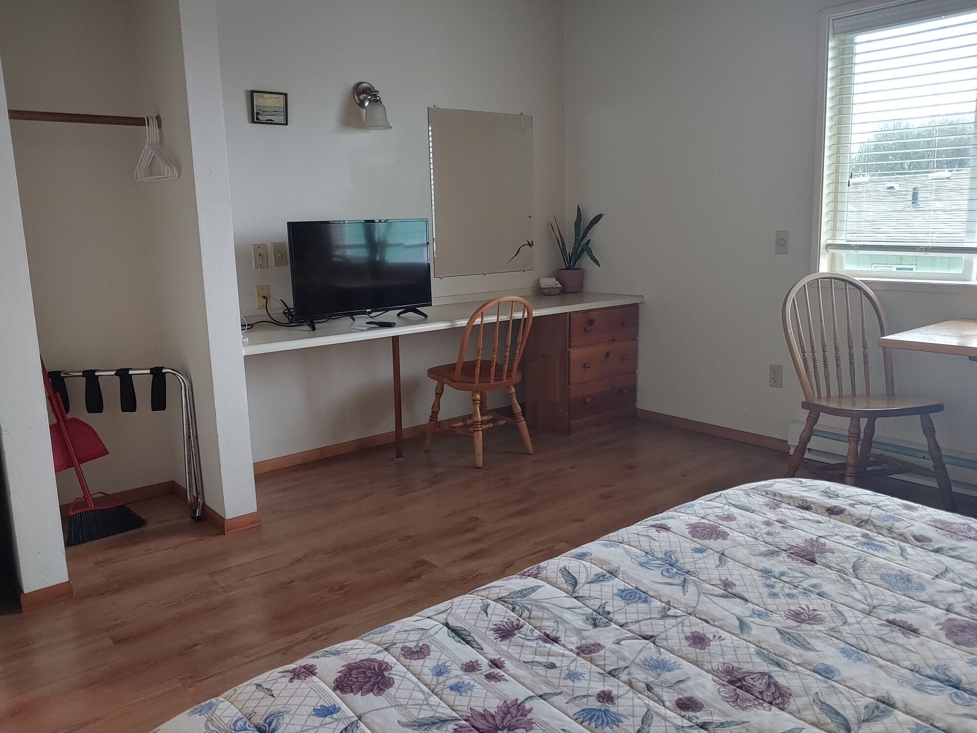 Une chambre à coucher avec un lit, un bureau avec un ordinateur, deux chaises, une fenêtre et une porte.