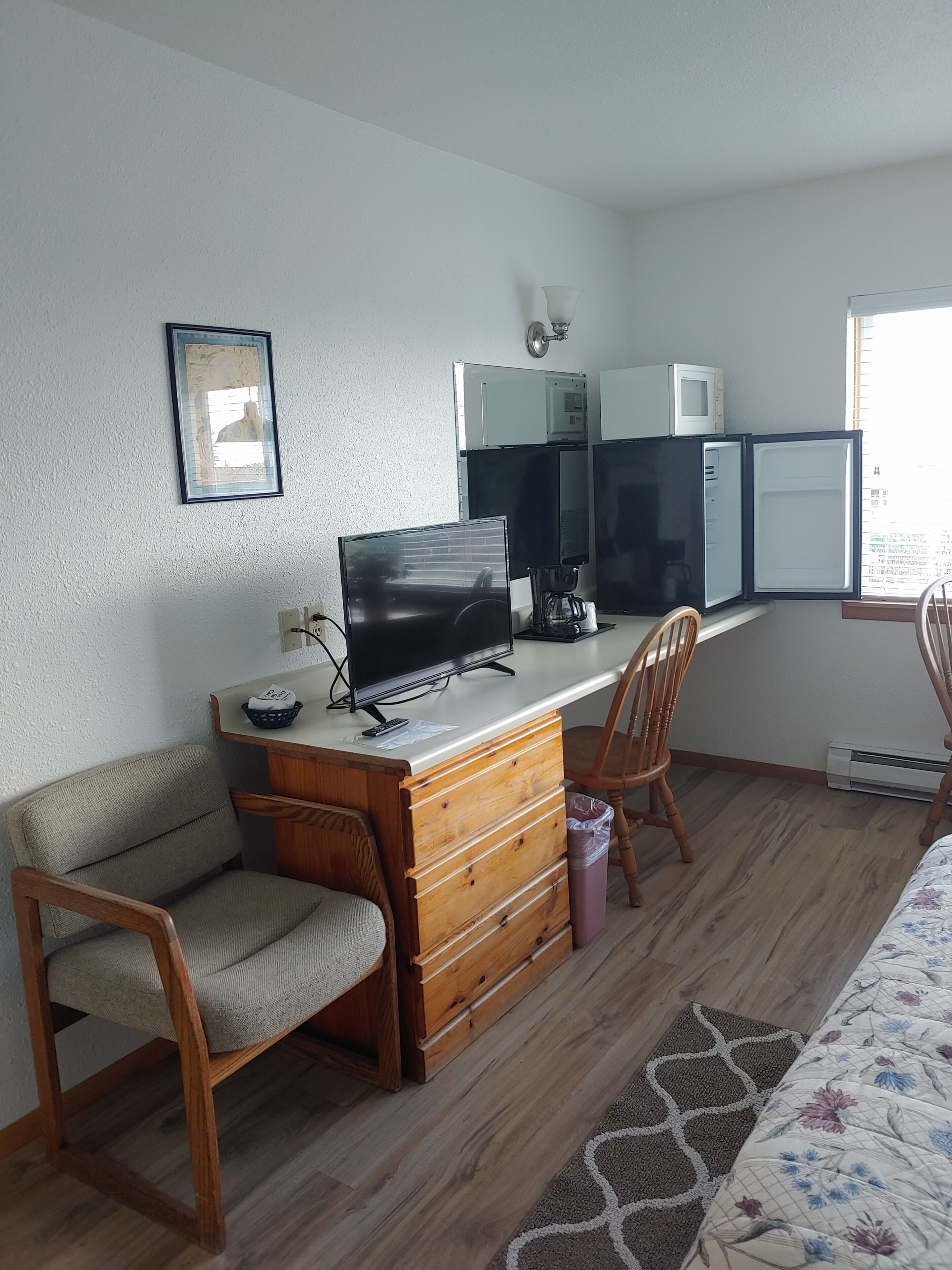 A room with a wooden desk, a television, a microwave, and a chair.