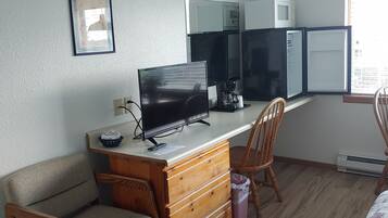 A room with a wooden desk, a television, a microwave, and a chair.