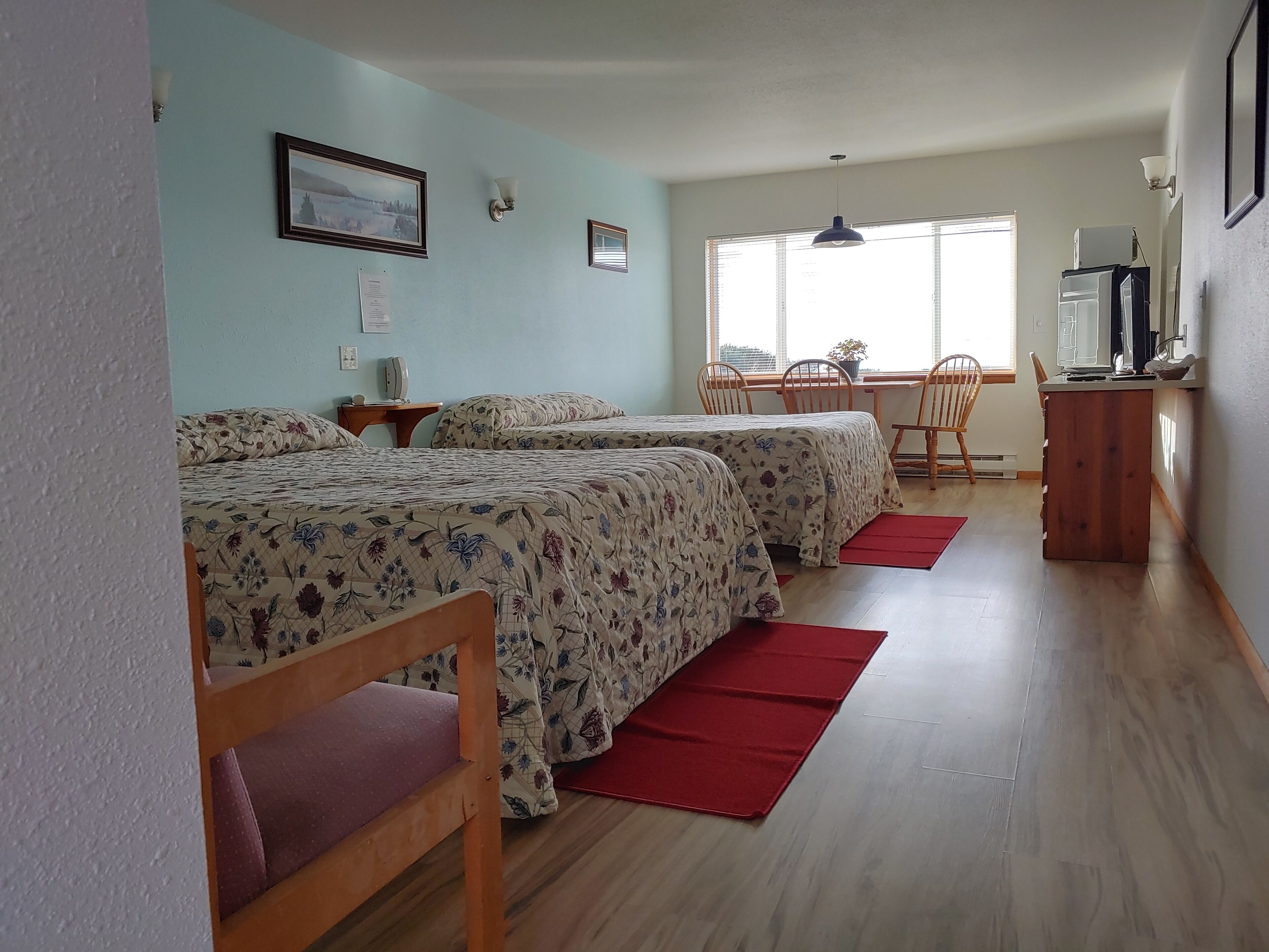 Une chambre avec deux lits, une table à manger avec des chaises, un téléviseur et une fenêtre avec des stores.