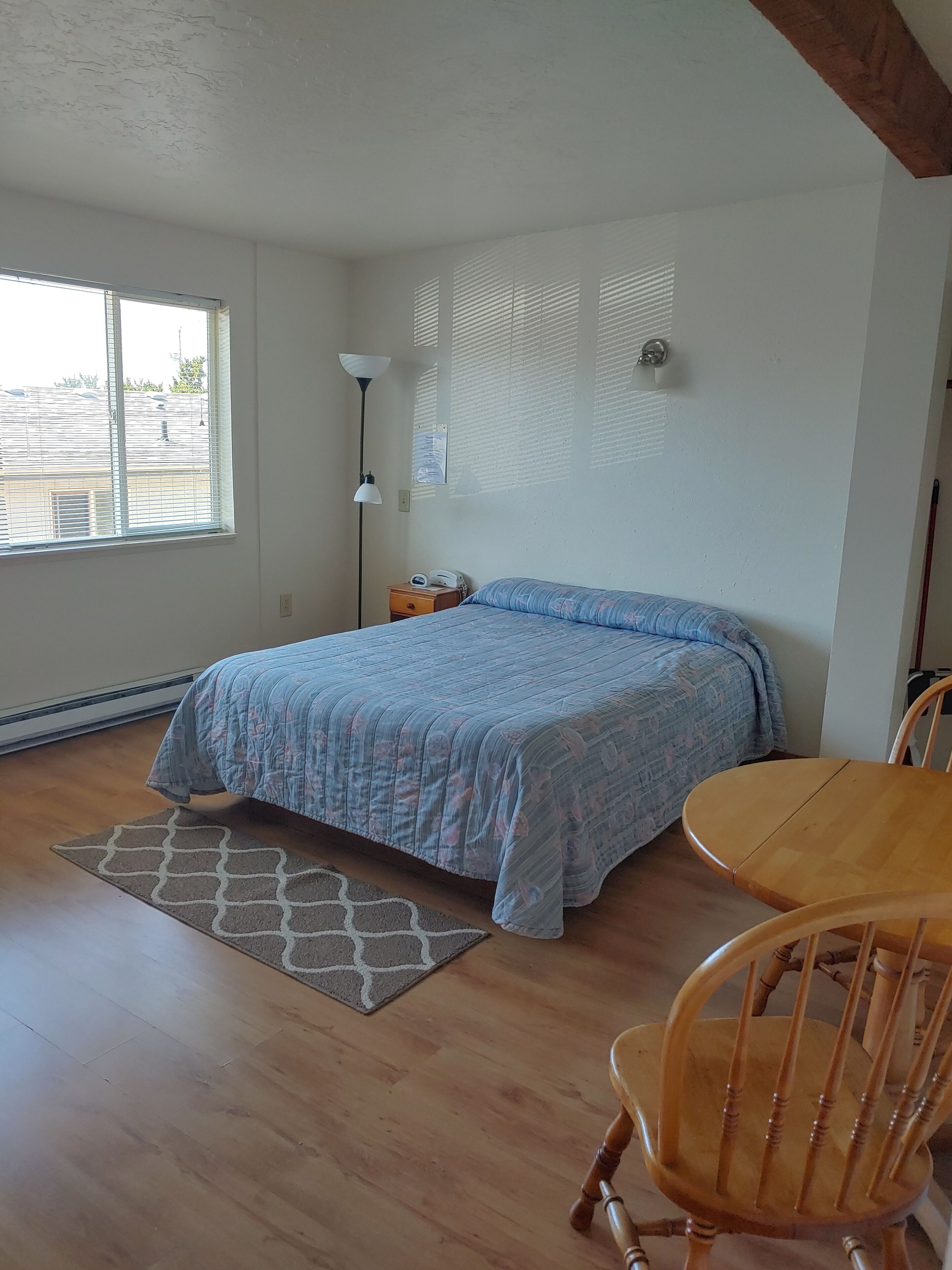 Un dormitorio con cama, mesita de noche, lámpara, silla y ventana con persianas.