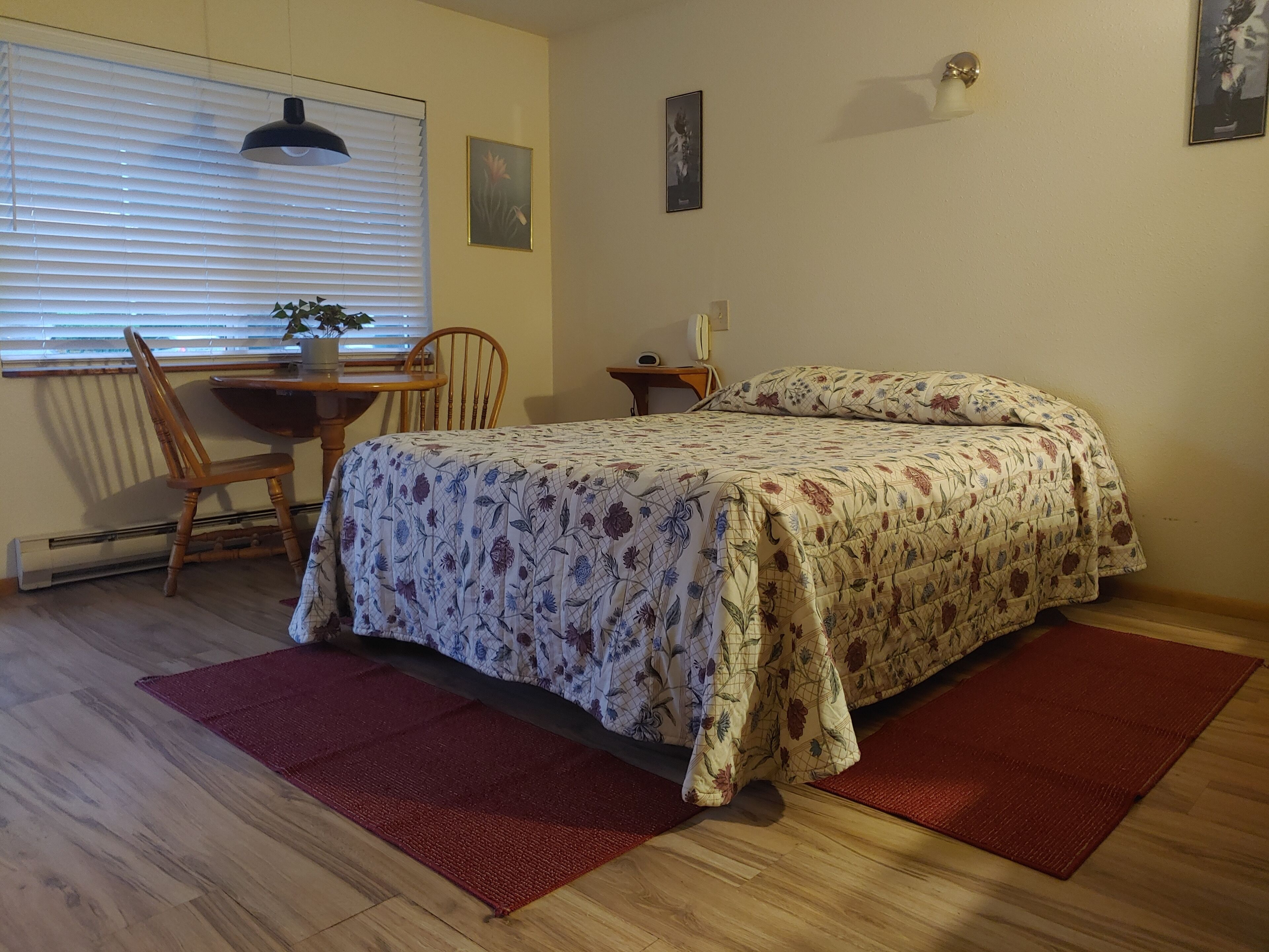 A bedroom with a bed, a desk, a chair, a radiator, and a window with blinds.