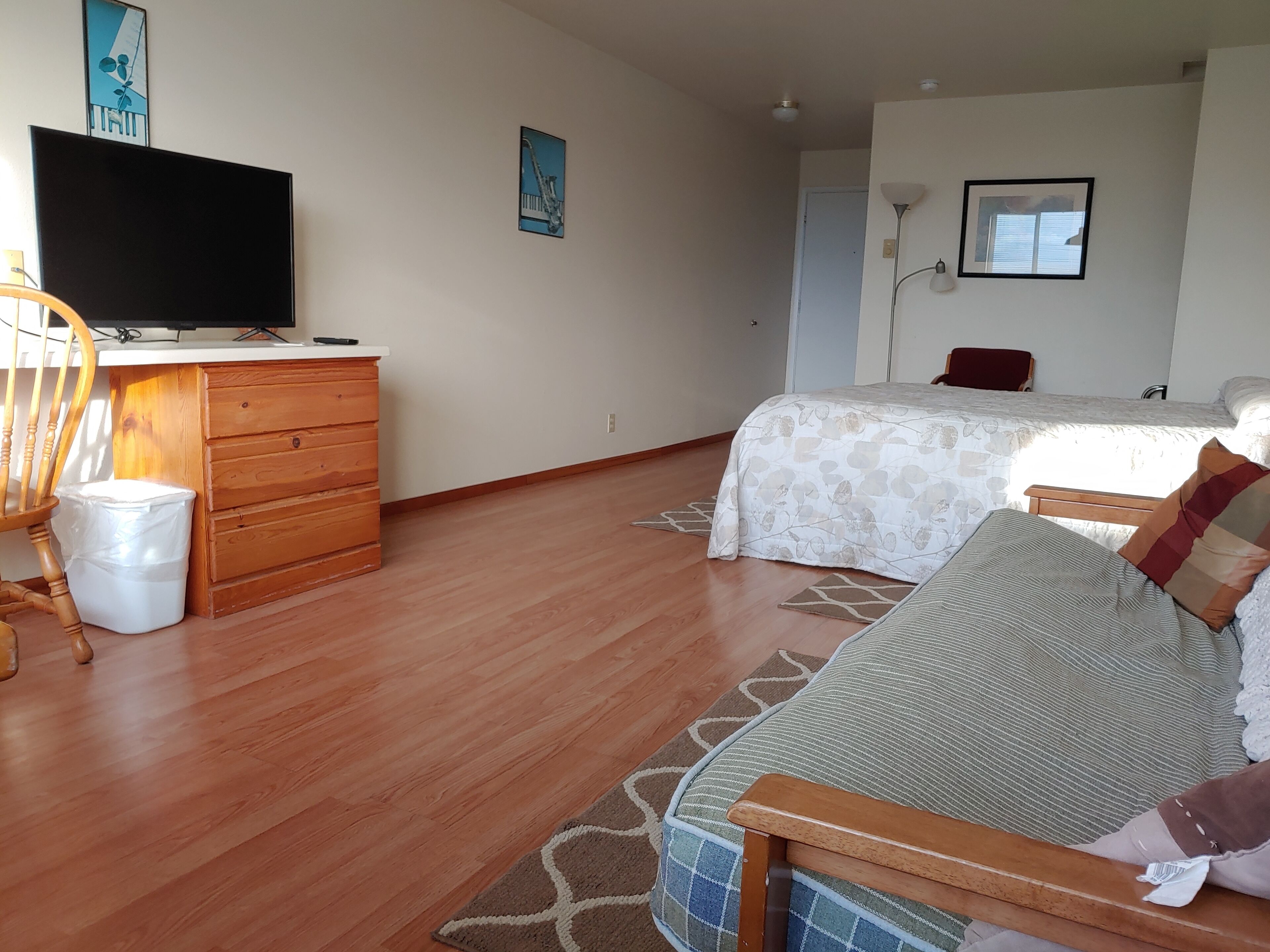 Une chambre à coucher comprenant un lit, un canapé, une commode en bois, un téléviseur et une poubelle.