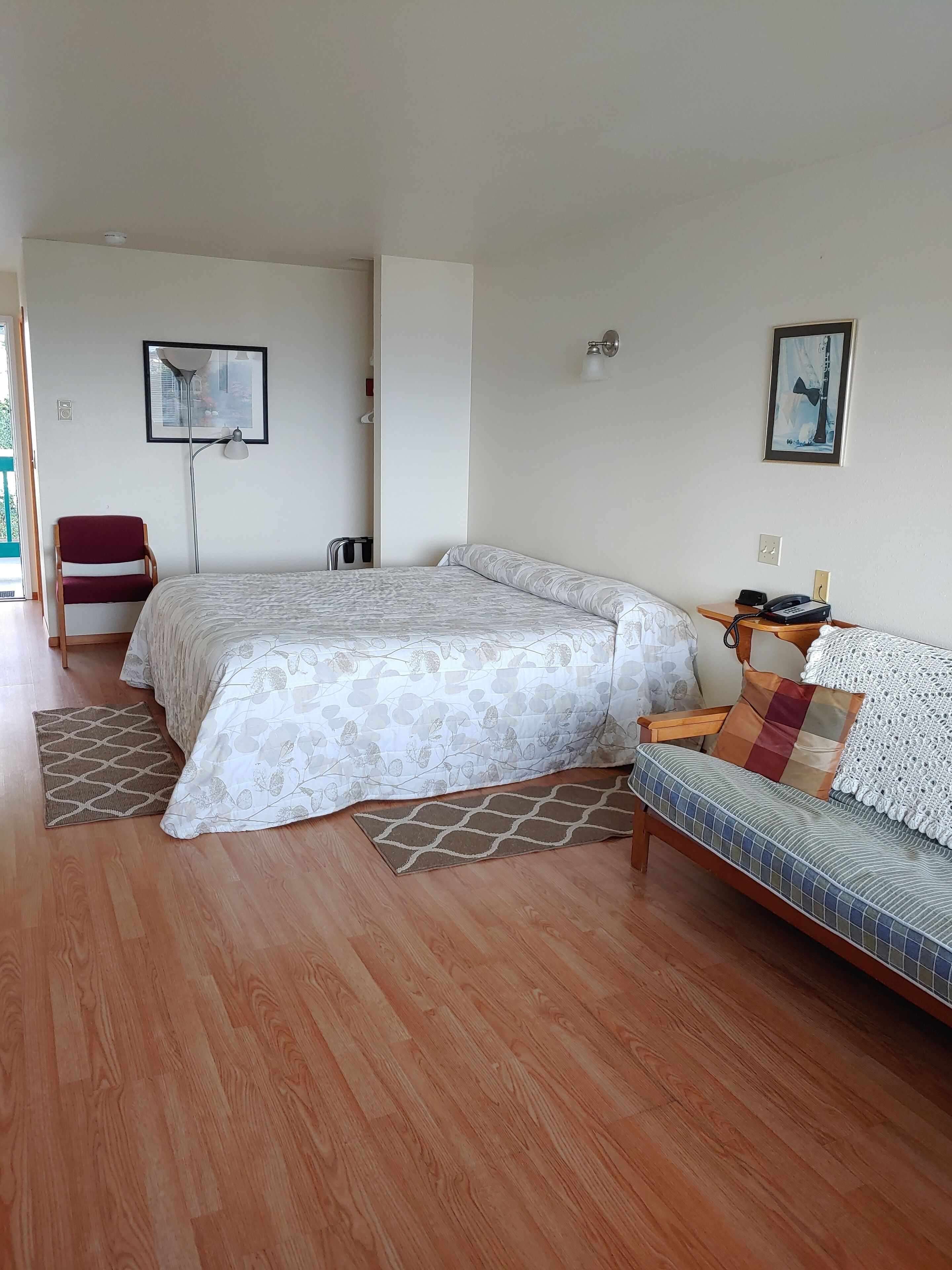 Un dormitorio con cama, sofá, silla, lámpara de pie y luz empotrada en la pared.