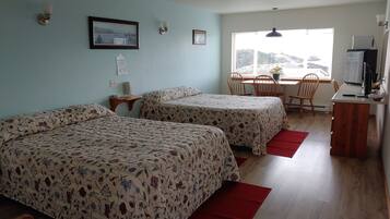 A room with two beds, a desk, a chair, a TV, and a window with blinds.