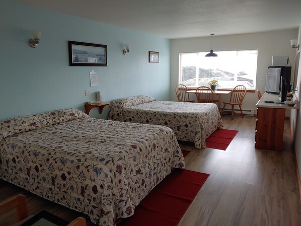 A room with two beds, a desk, a chair, a TV, and a window with blinds.