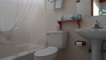 Un baño con inodoro, lavamanos, cortina de ducha y estante con artículos de aseo.