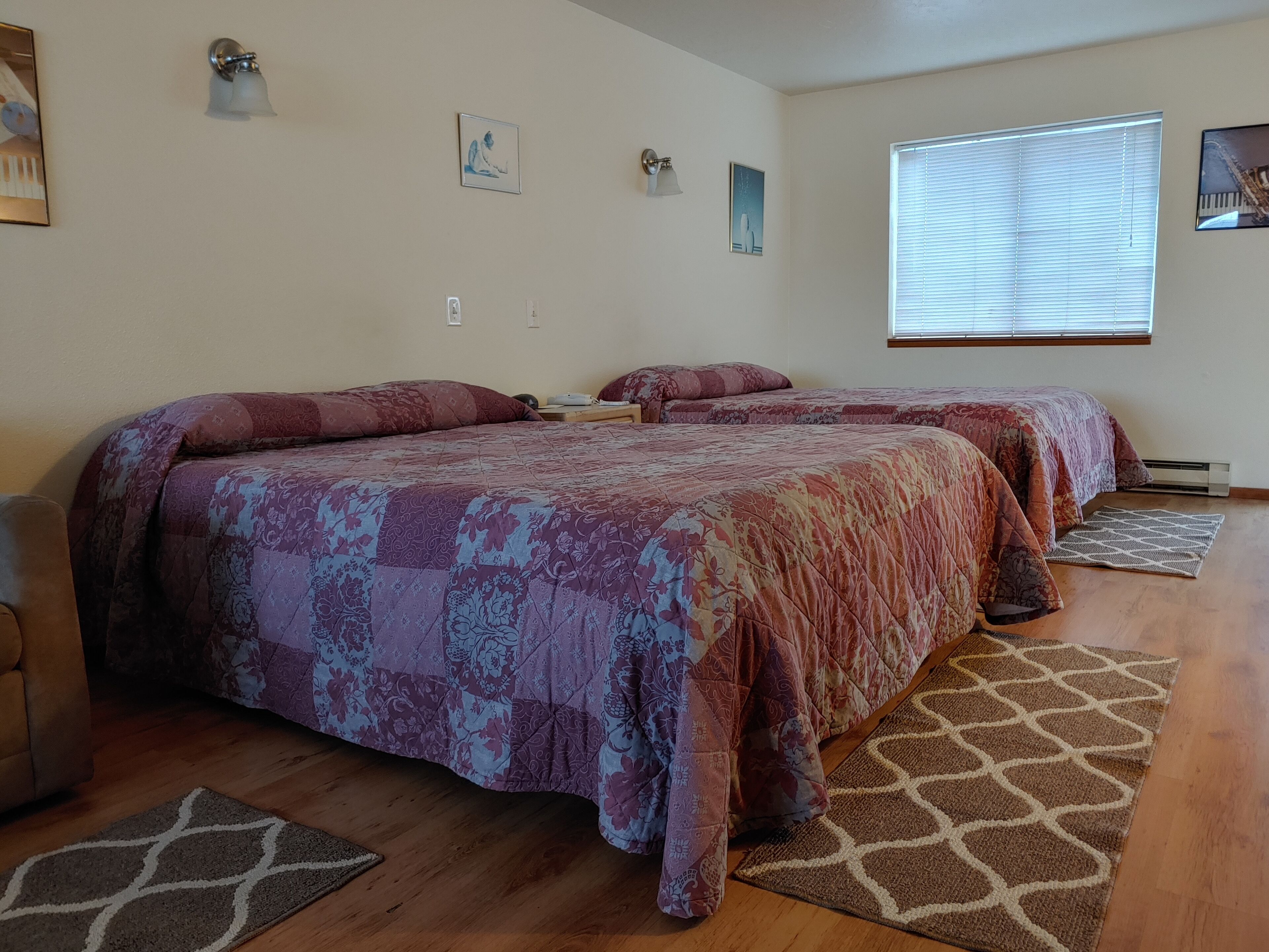A bedroom with two beds, wooden flooring, and a window with blinds.