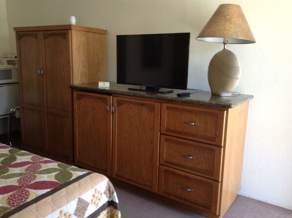 A bedroom with a wooden cabinet, a television, and a lamp. - Independence Courthouse Motel (Independence)