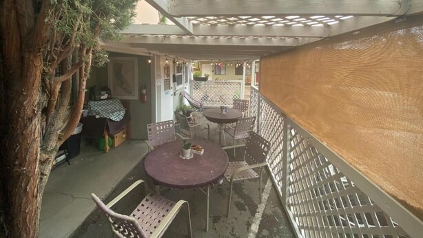 Un espacio al aire libre techado con mesas y sillas, un árbol y un muro de madera.