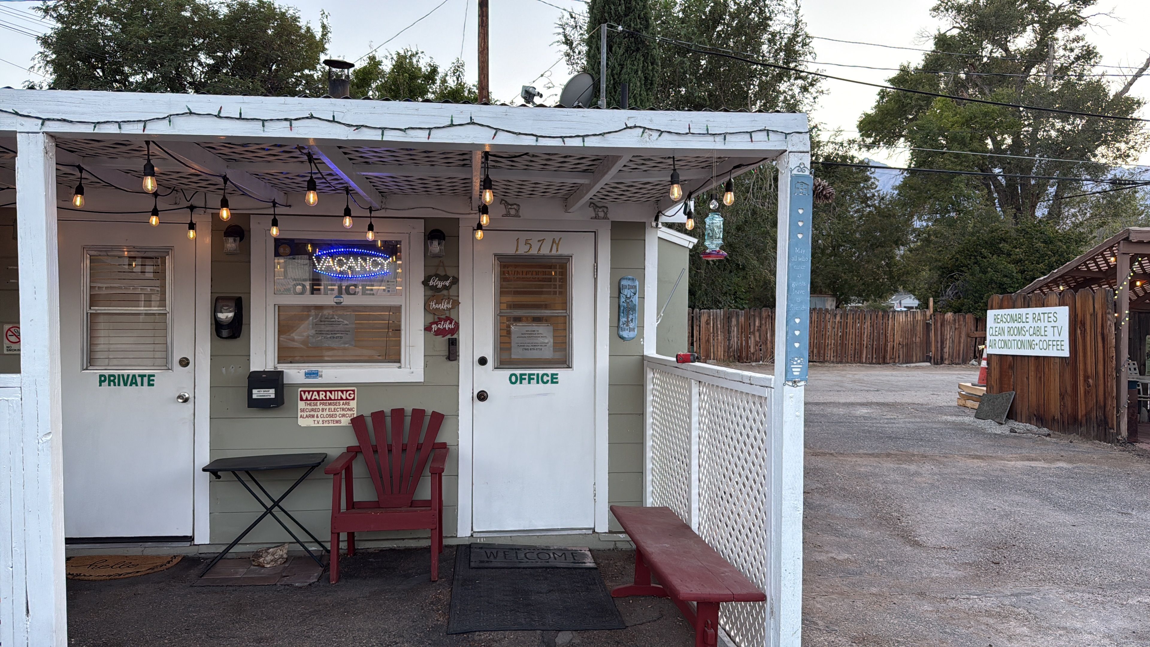 A small, private office with a neon sign, a red chair, and a bench outside.