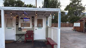 A small, private office with a neon sign, a red chair, and a bench outside.