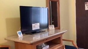 Un escritorio de madera con un televisor, un letrero pequeño y un espejo.