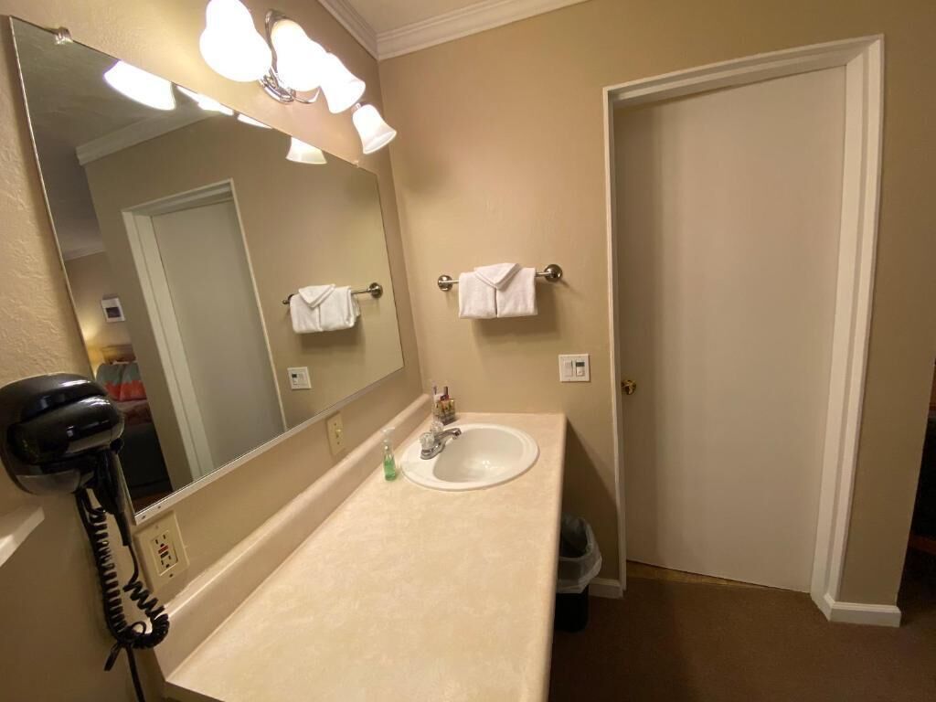 Bagno con lavandino, specchio e asciugacapelli. Asciugamani appesi al muro e cestino nell'angolo.