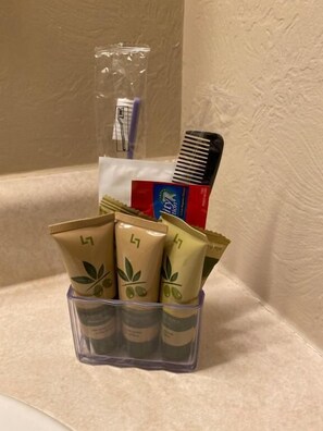 A bathroom sink with toiletries including a toothbrush, comb, and several tubes of lotion. - Independence Courthouse Motel (Independence)
