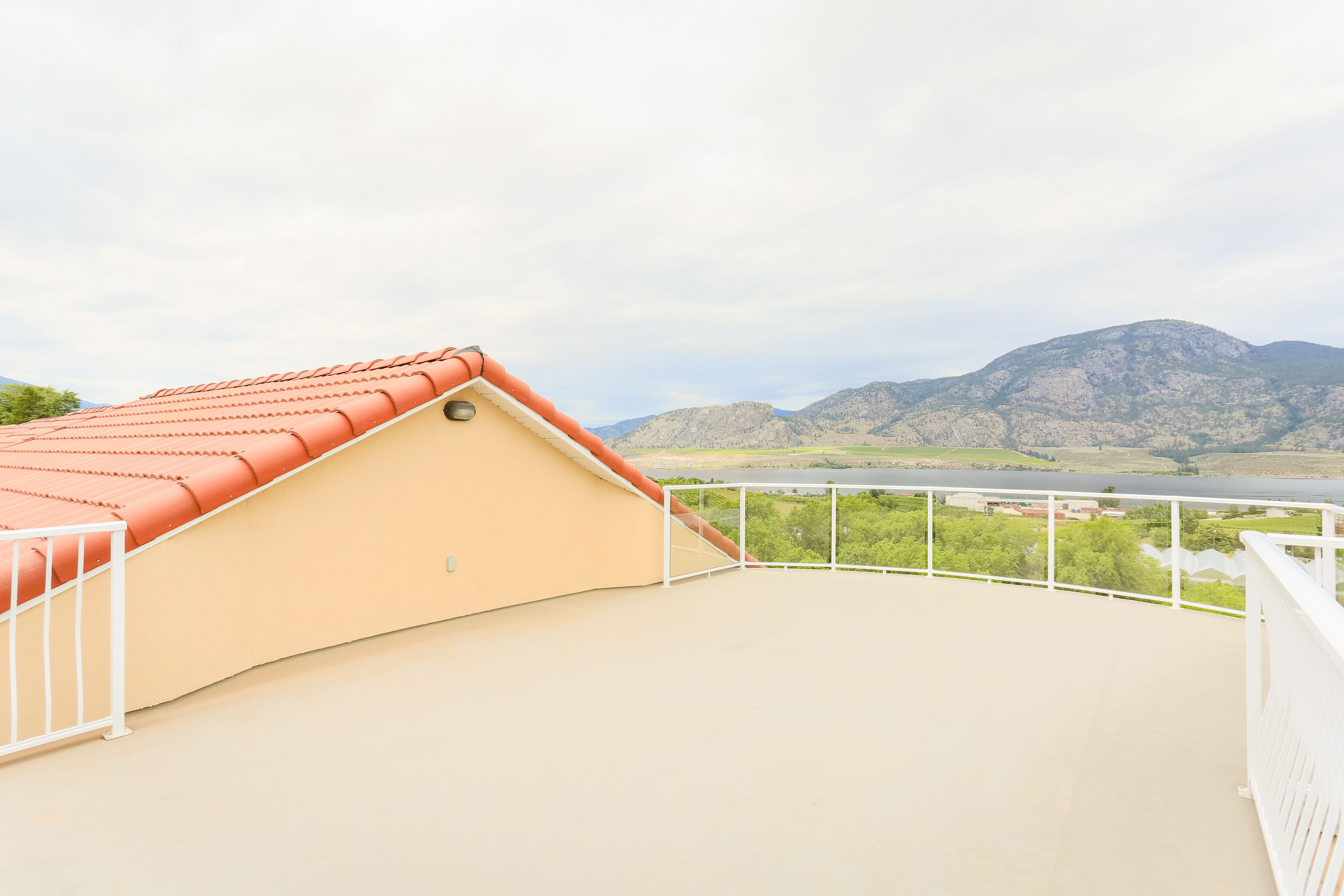 A rooftop terrace with a curved roof, white railing, and a view of mountains and a river.