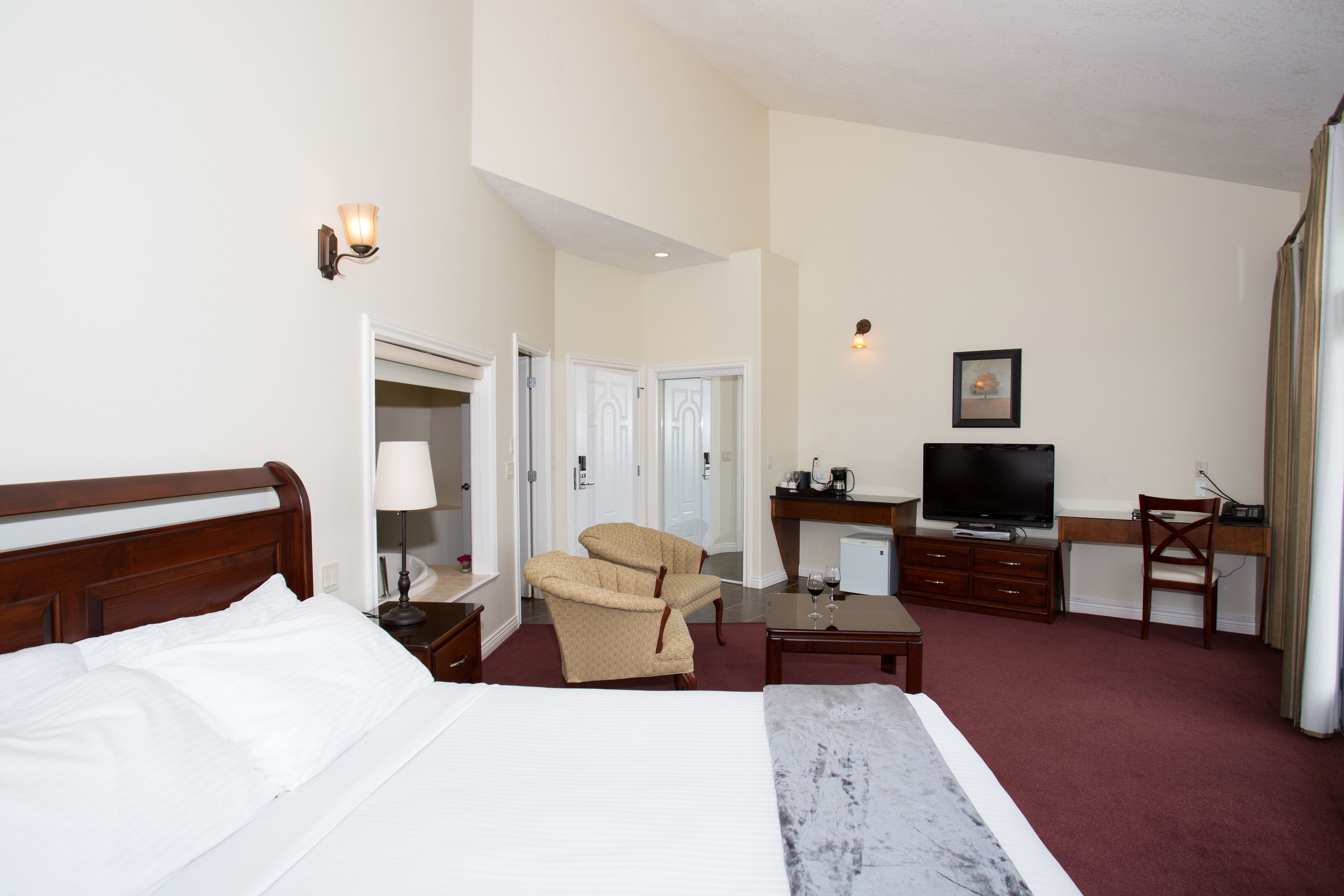 A hotel room with a bed, a desk with a television, a chair, and a small table with a wine glass.