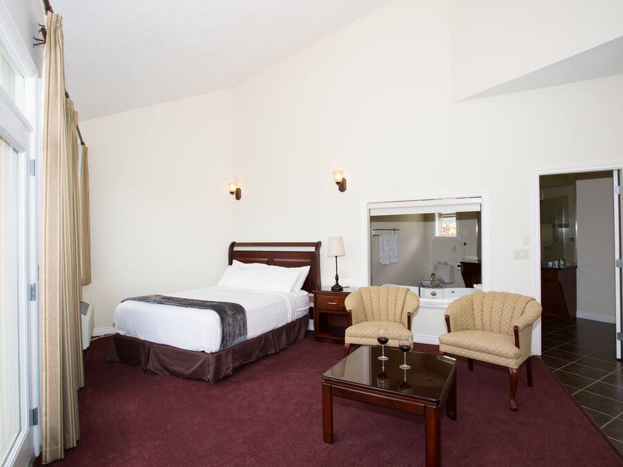 A hotel room with a bed, two armchairs, a coffee table, a nightstand, a lamp, and a bathroom visible through an open door.