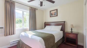 A bedroom with a bed, a nightstand, a ceiling fan, a window with curtains, and a picture on the wall.