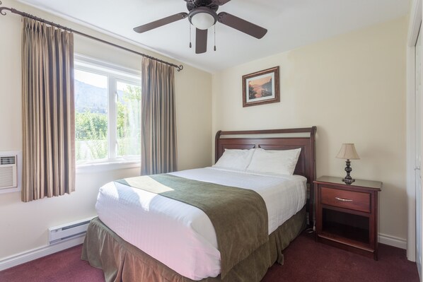 A bedroom with a bed, a nightstand, a ceiling fan, a window with curtains, and a picture on the wall.
