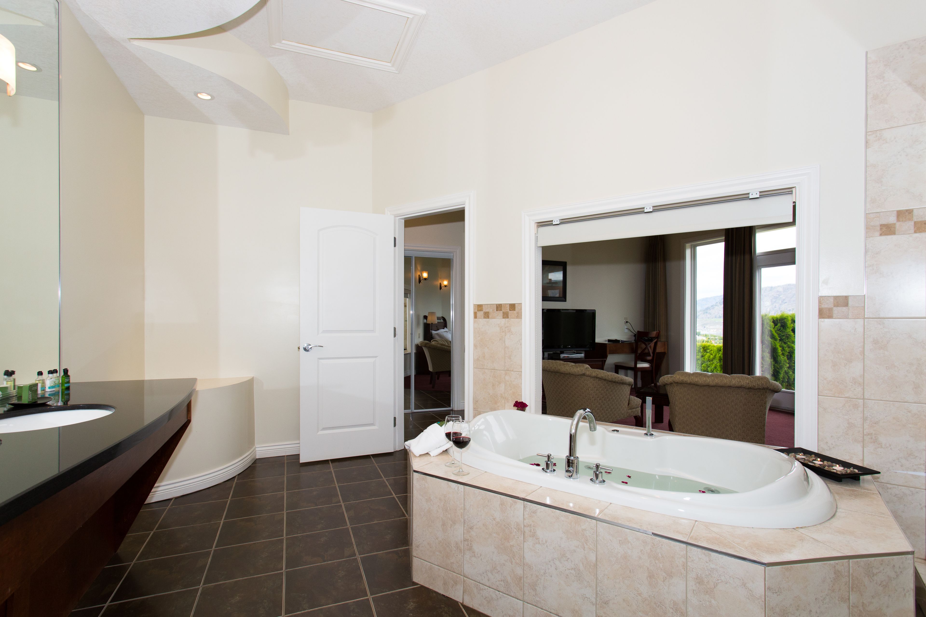A modern bathroom with a large bathtub, a glass-enclosed vanity, and a large mirror.