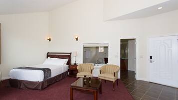 Una habitación de hotel con cama, dos sillones, una mesita con copas de vino, una mesita de noche y un espejo.