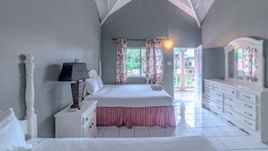 A bedroom with a large bed, a dresser, a nightstand, and a mirror. - Jamaica Tamboo Resort (Negril)