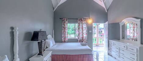 A bedroom with a large bed, a dresser, a nightstand, and a mirror.