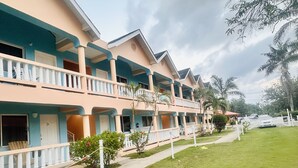 A multi-story hotel with balconies, a well-maintained lawn, and a clear sky. - Jamaica Tamboo Resort (Negril)
