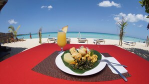 A table with a red tablecloth, a plate of food, a glass of orange juice, and a view of the beach and ocean. - Jamaica Tamboo Resort (Negril)