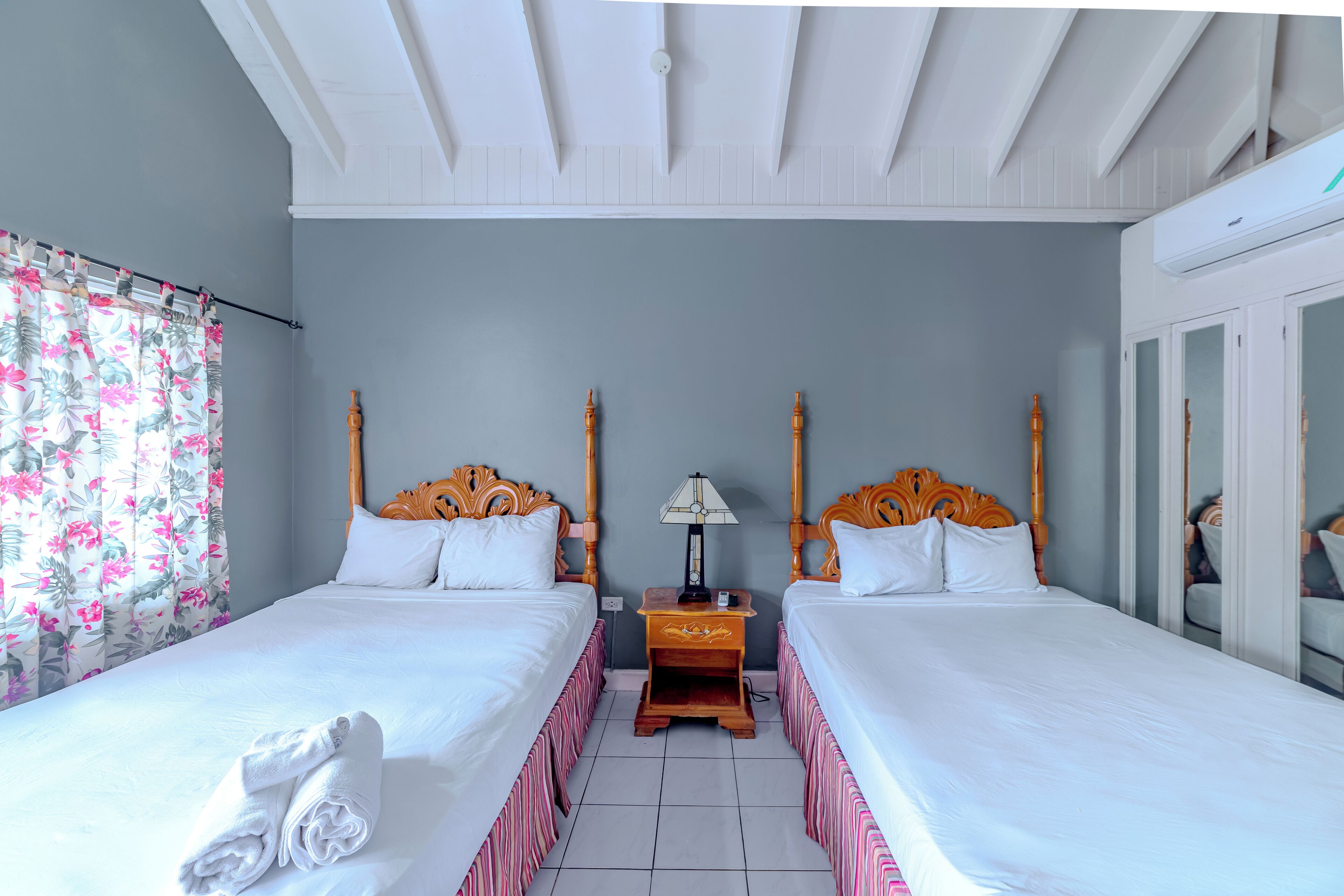 A hotel room with two beds, a wooden headboard, a nightstand with a lamp, and a large mirror.