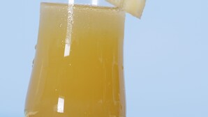 A glass of yellow beverage with a pineapple garnish on a red surface. - Jamaica Tamboo Resort (Negril)