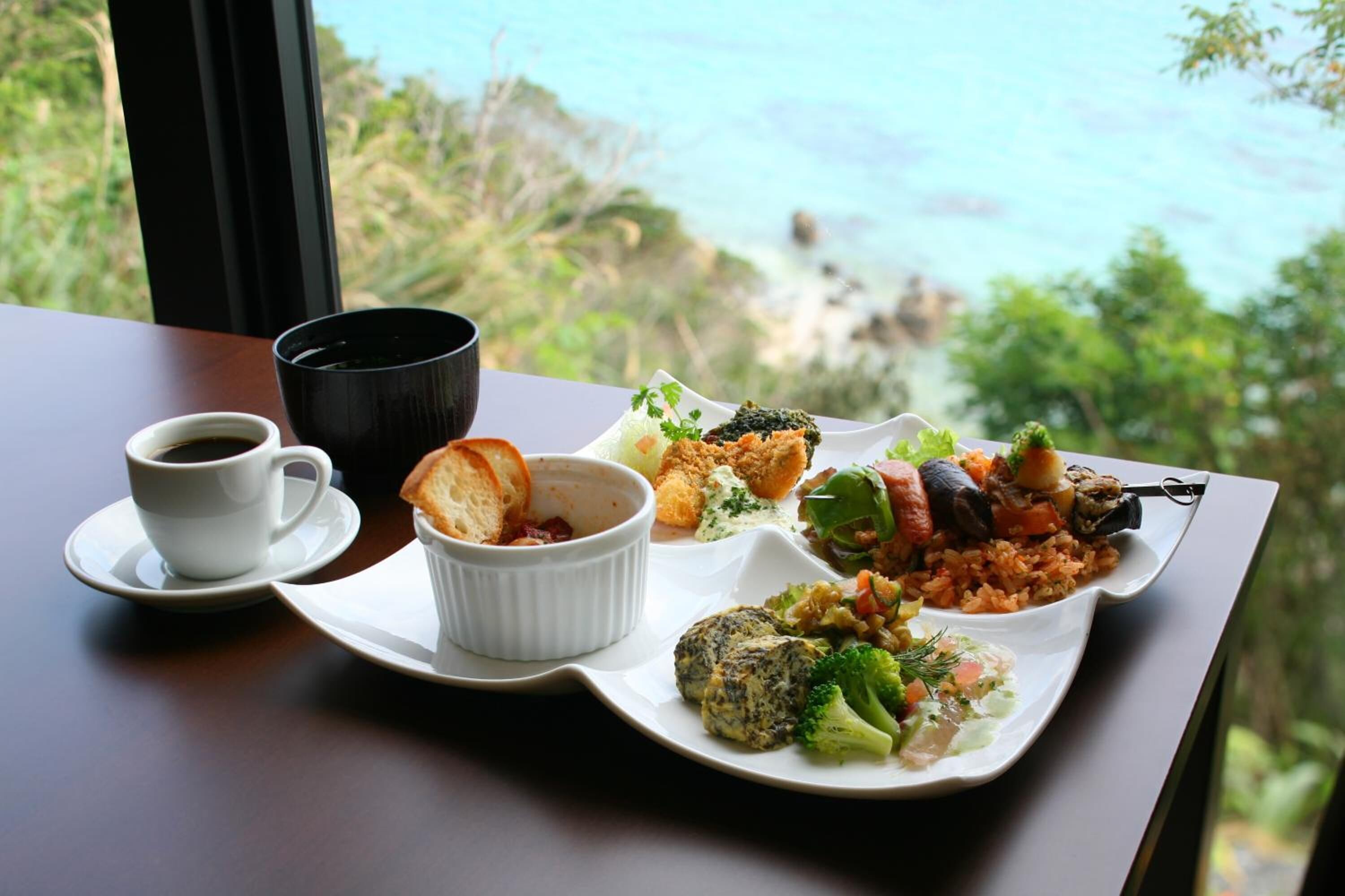 A table with a variety of dishes, a cup of coffee, and a scenic view of the ocean.