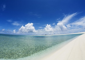 Una playa con agua turquesa cristalina y arena blanca, bajo un cielo azul con nubes dispersas.