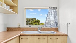 A kitchen with a sink, wooden cabinets, and a window with a view of greenery. - Avondale Motor Inn (Auckland)